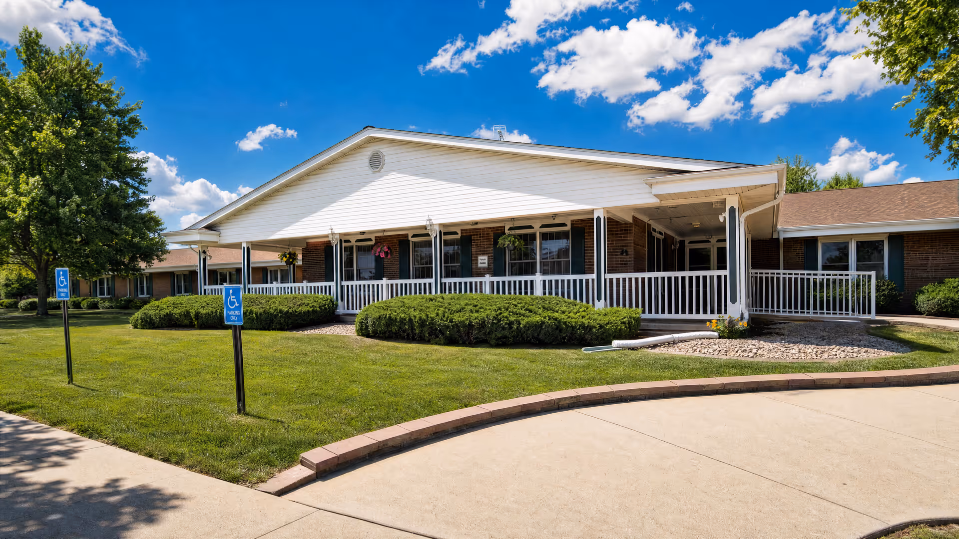 Exterior view of Willow Dale Wellness Village Care Center with white porch, lawn, and sky.