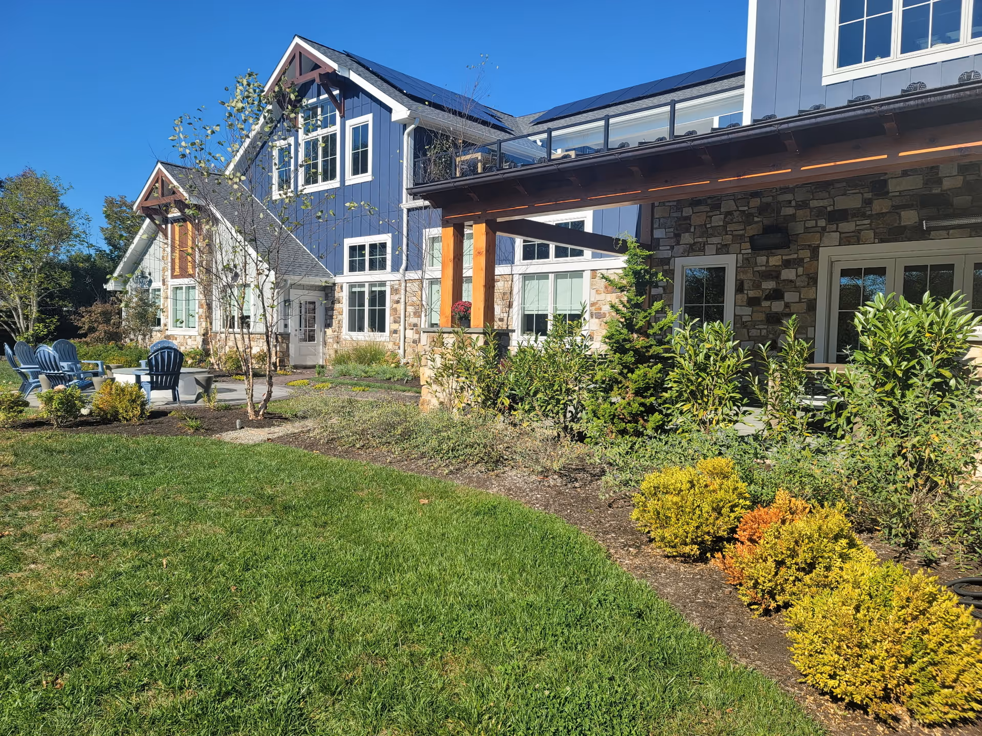 Blue siding senior living facility with stone accents and sunny outdoor seating area.
