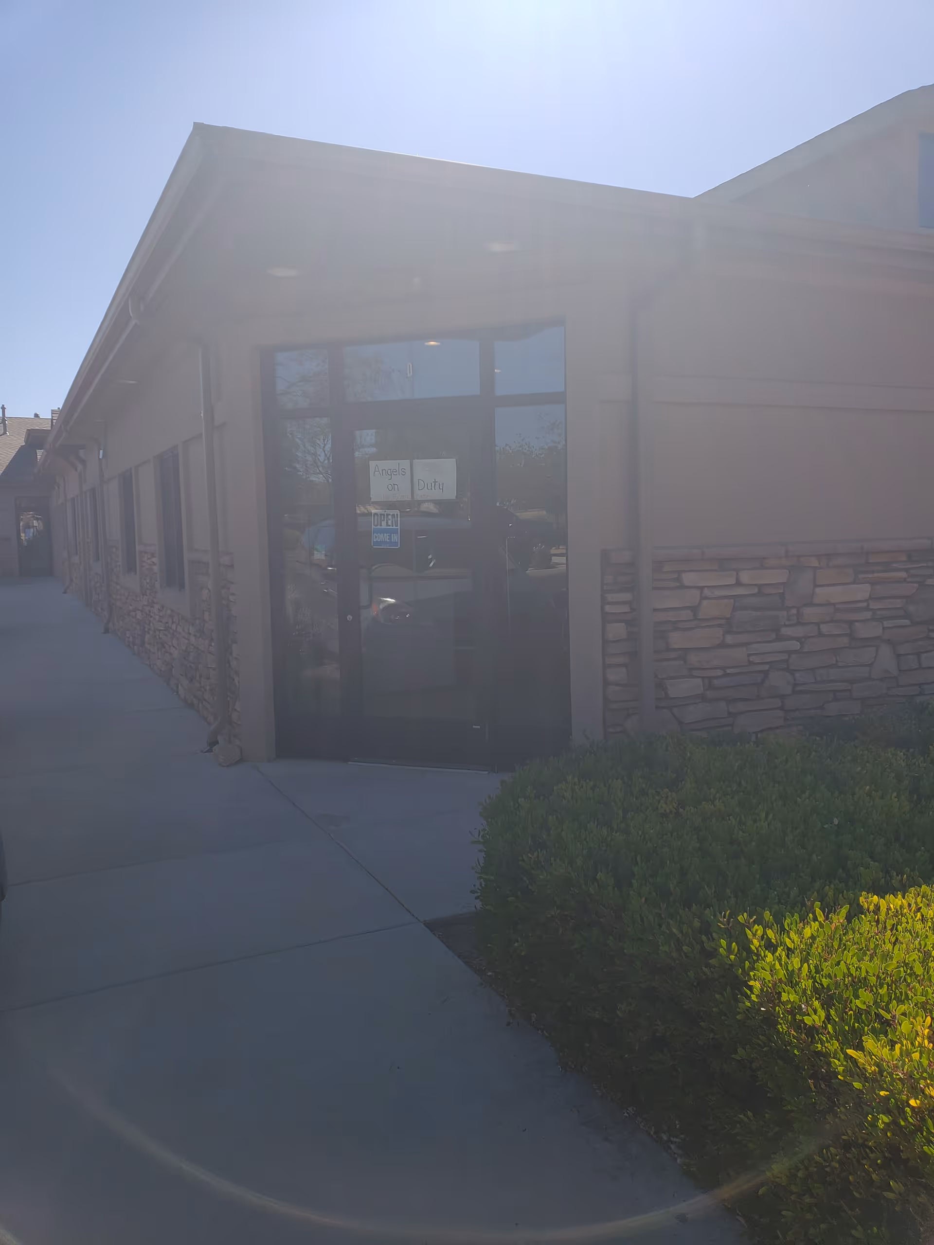Sunlit entrance to Angels On Duty facility with glass doors and stone facade.