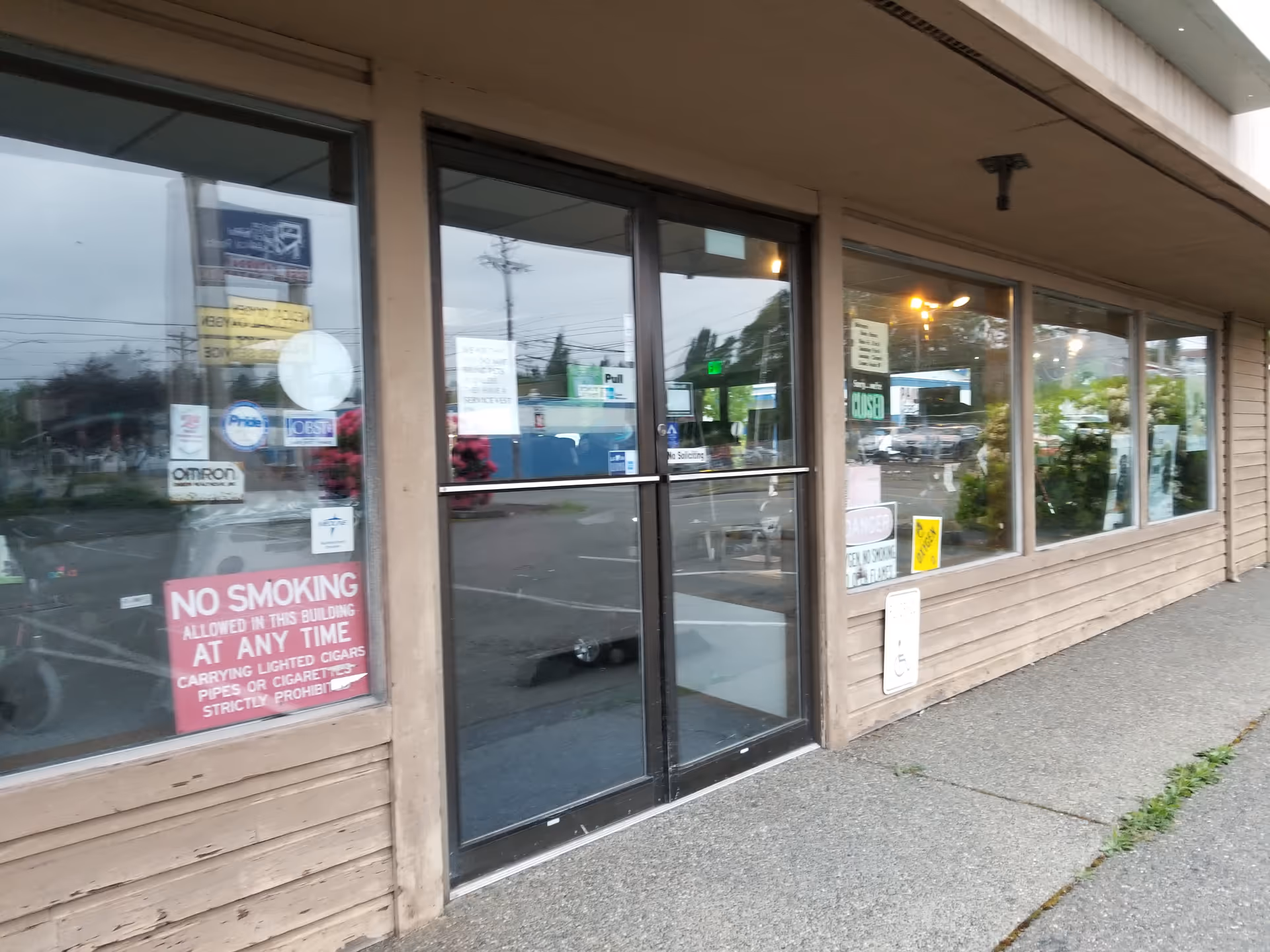 Storefront with large glass doors and windows, wooden siding, and various sign stickers.