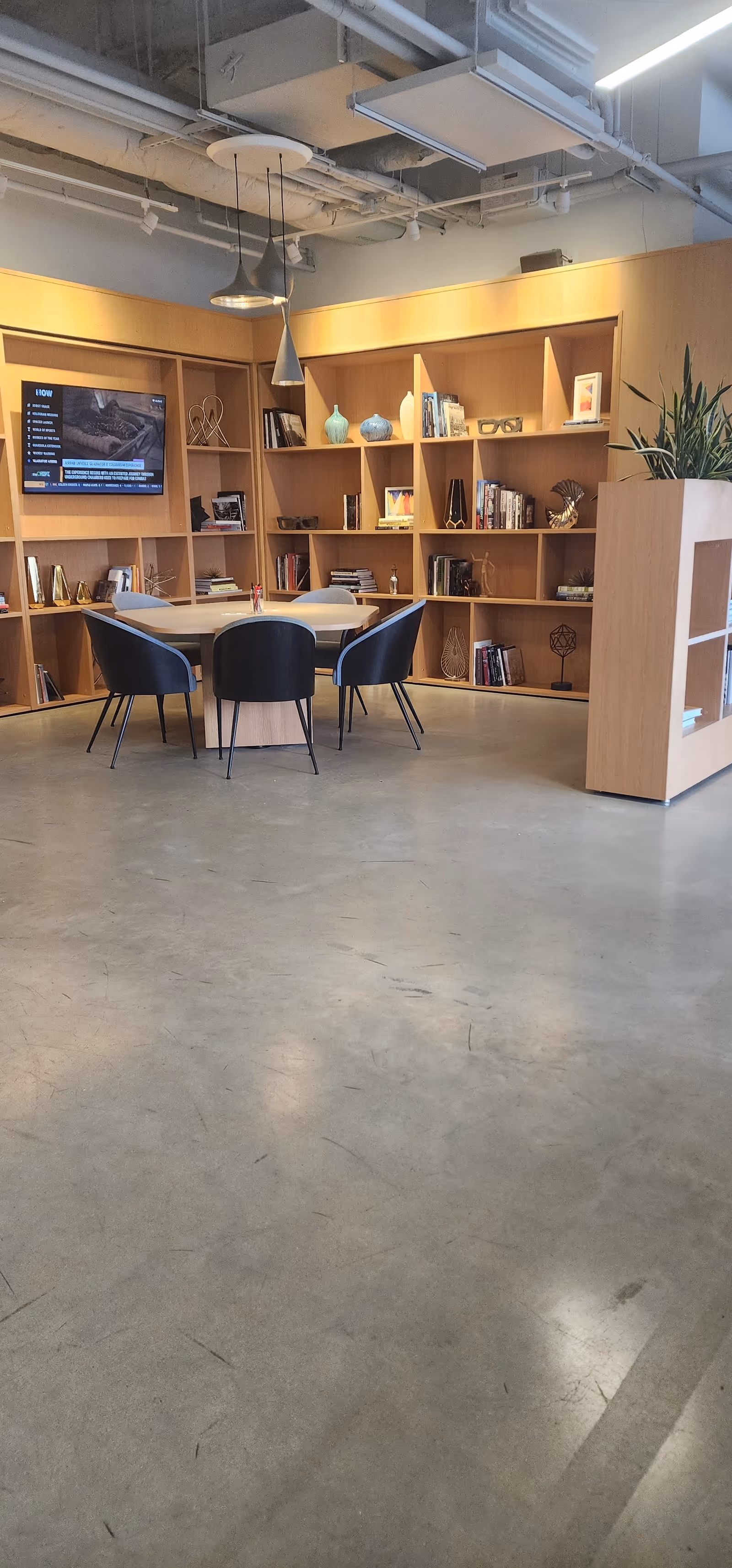 Modern interior lounge with a round table, blue chairs, bookshelves, and a wall-mounted TV.