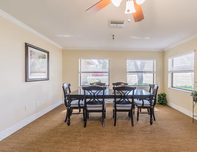 Bright dining room with a dark wood table, six chairs, and large windows.