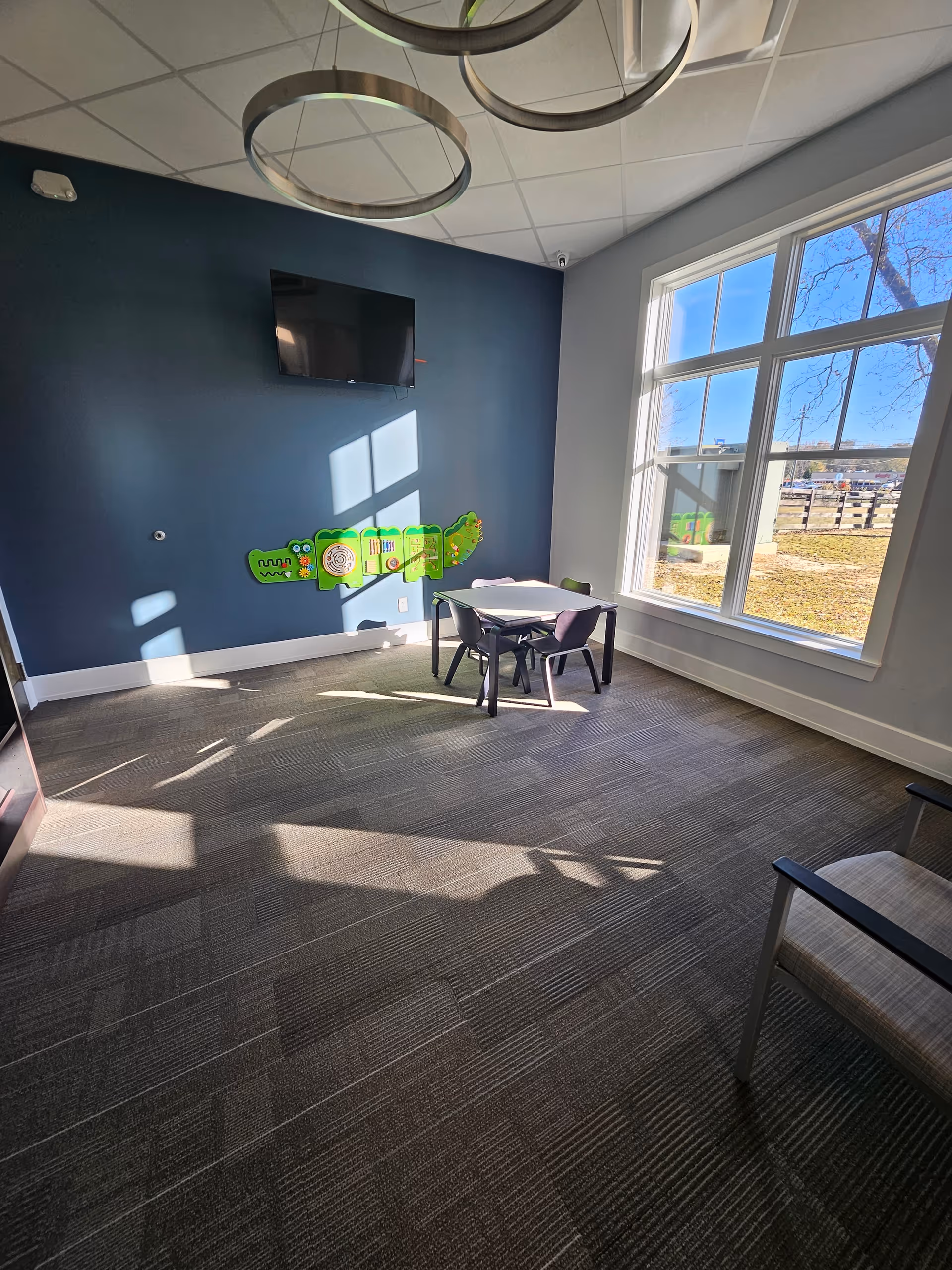 Bright activity room with blue accent wall, wall art, a table and chairs, and large window.