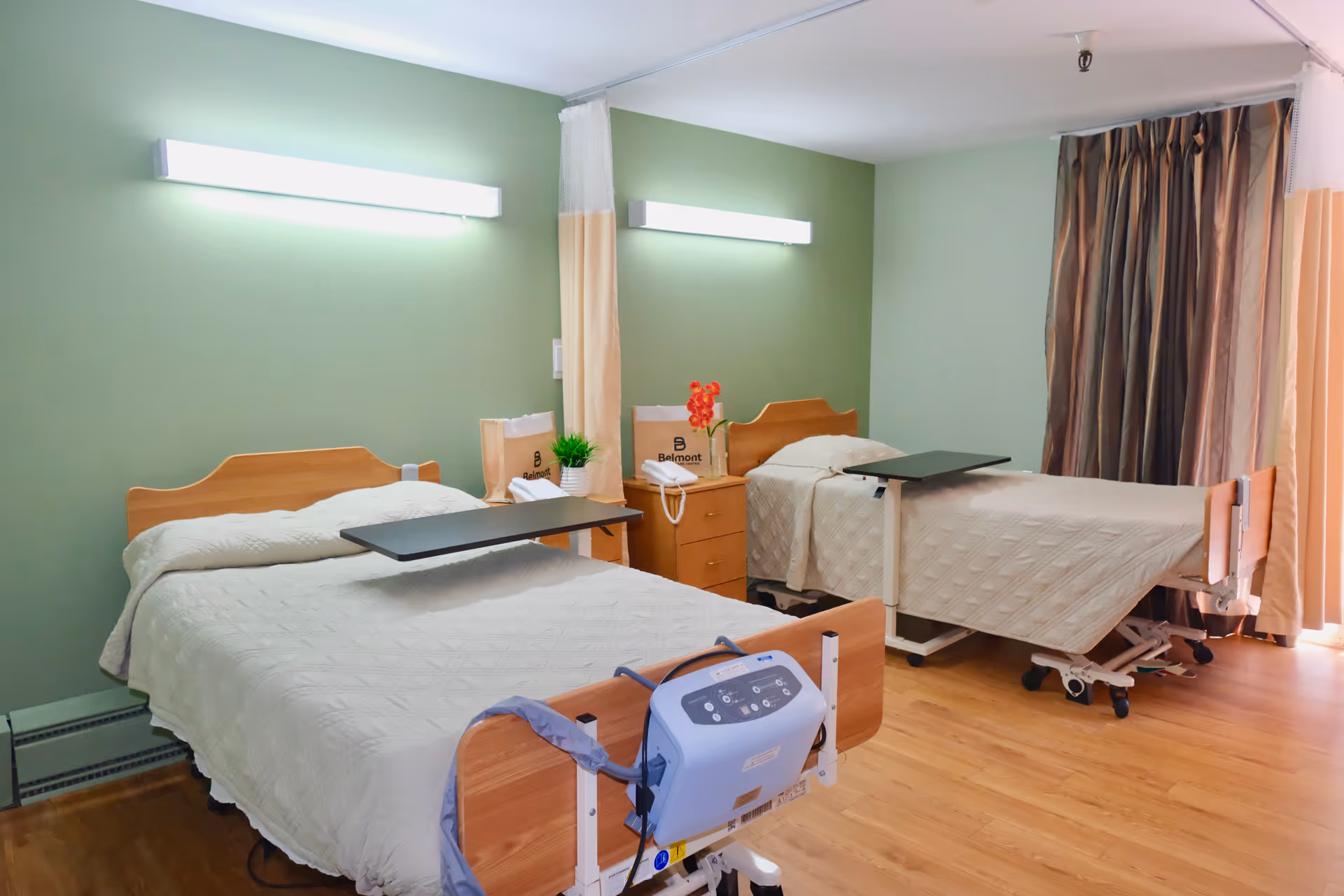 Two hospital-style beds in a green-walled patient room with shared nightstand and curtains.