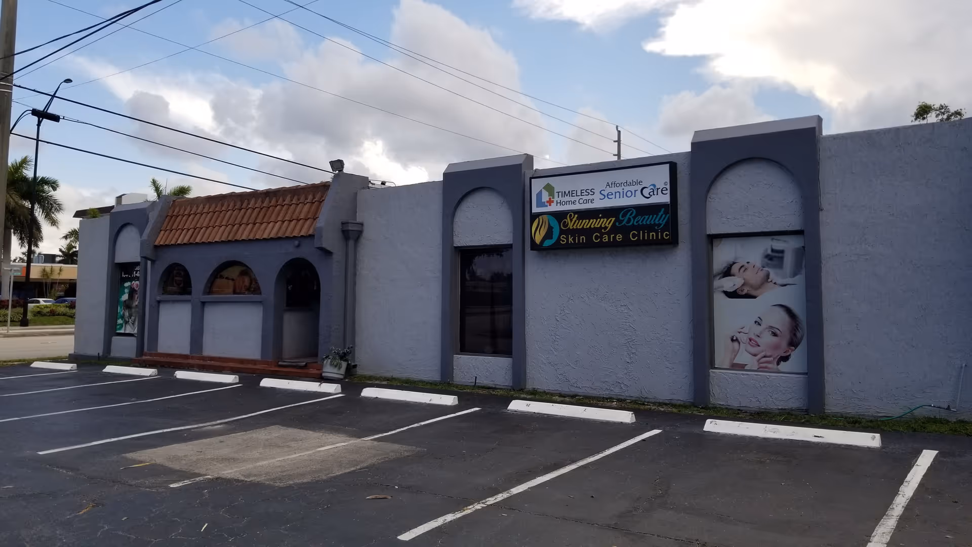 Gray, single-story building facade with multiple business signs and a parking lot.
