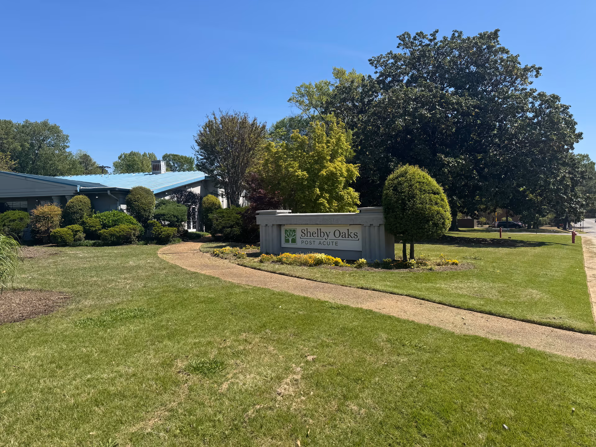 Front yard of Shelby Oaks Post Acute building with landscaped lawn and curved walkway.