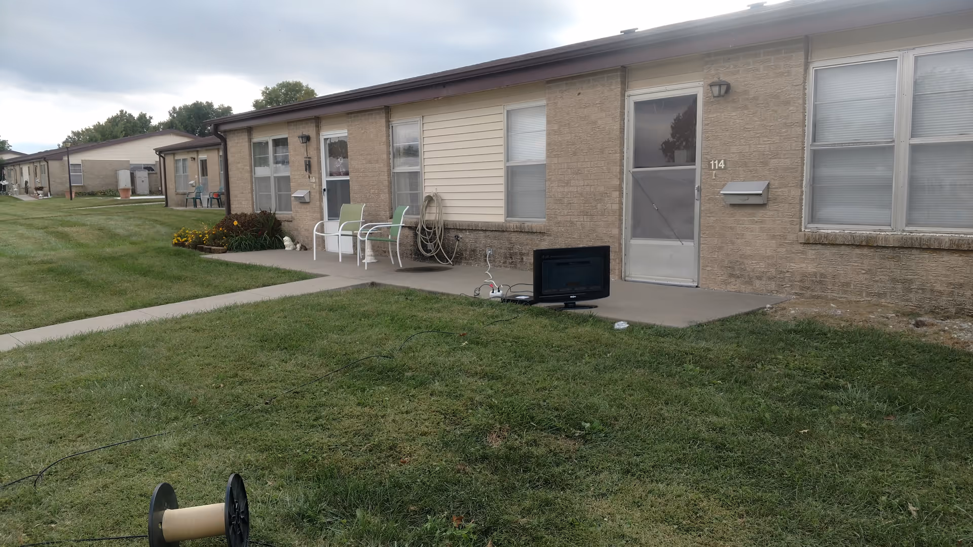 Row of single-story senior housing units with small outdoor seating and a TV.