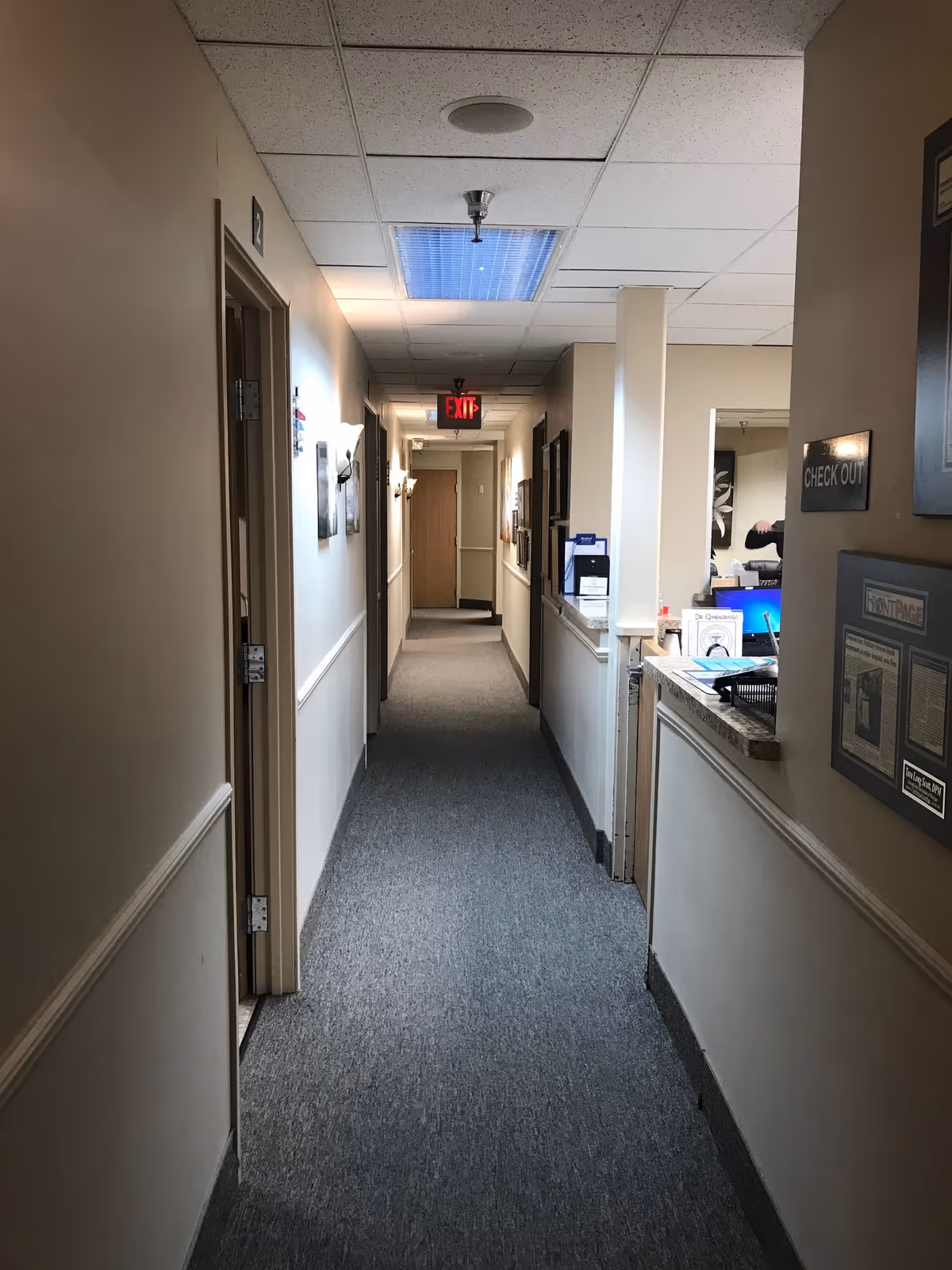 Long hallway in a senior facility with a front desk and exit sign at far end.