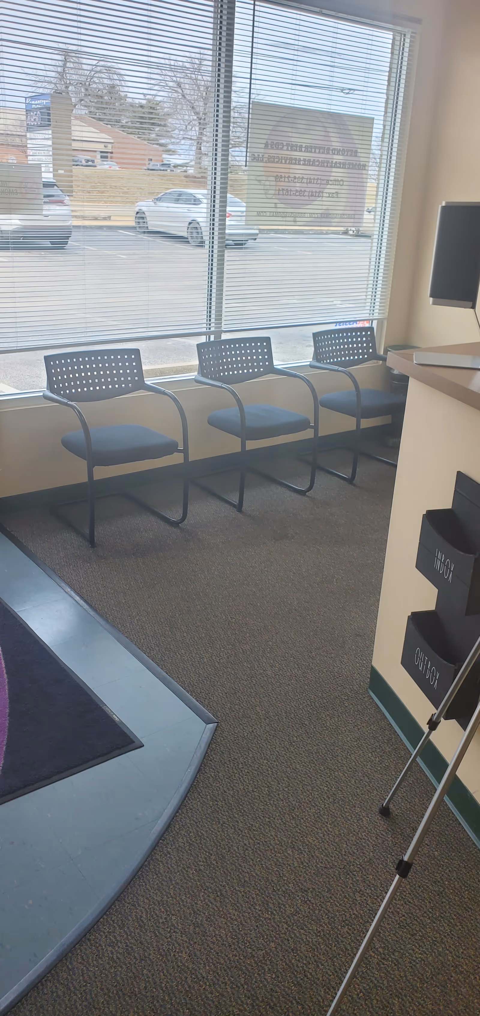 Lobby area with four metal chairs by a large window, blinds, and a reception counter.