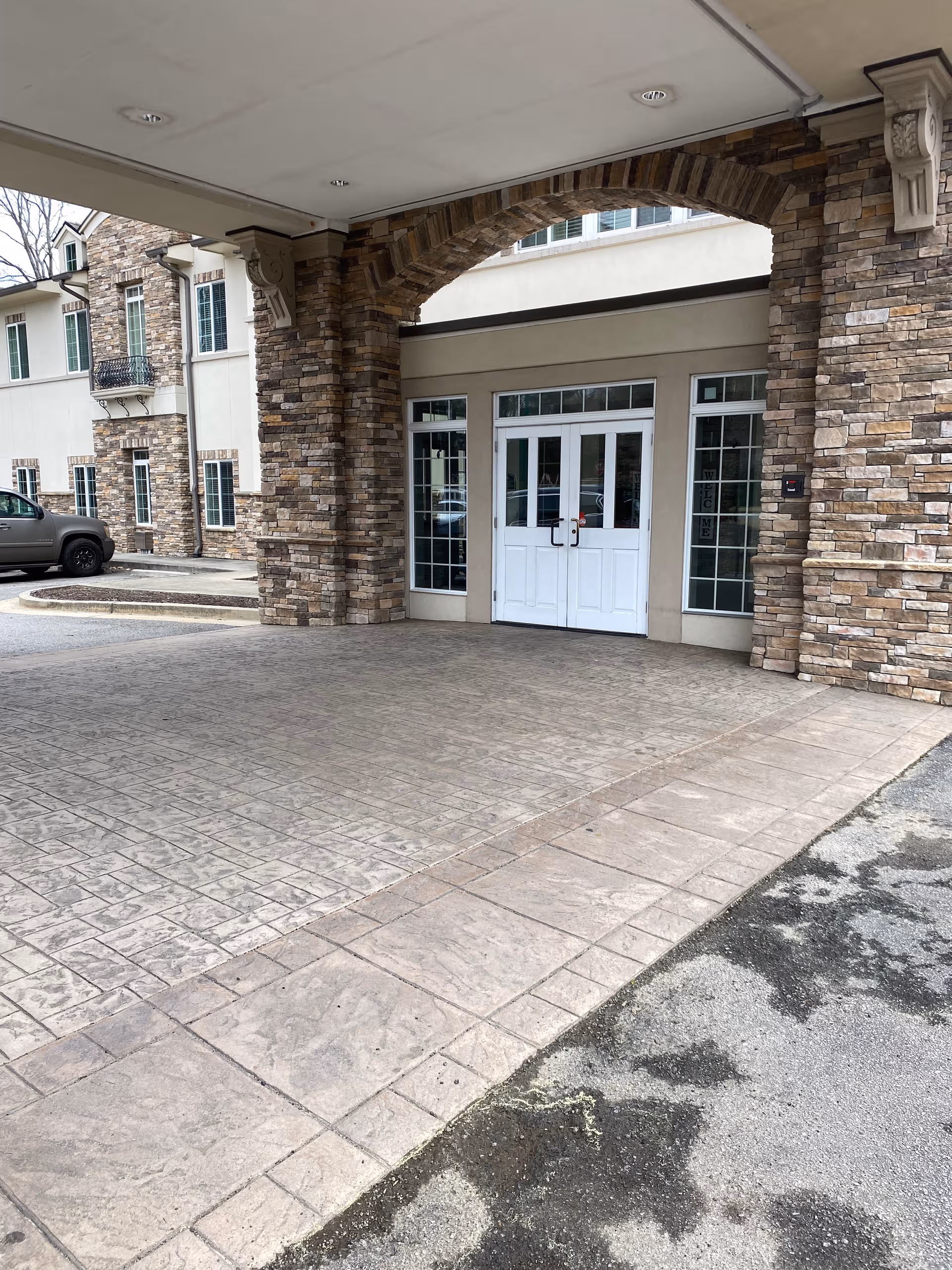 Stone archway entrance with white doors under a covered, brick-accented porte-cochere.