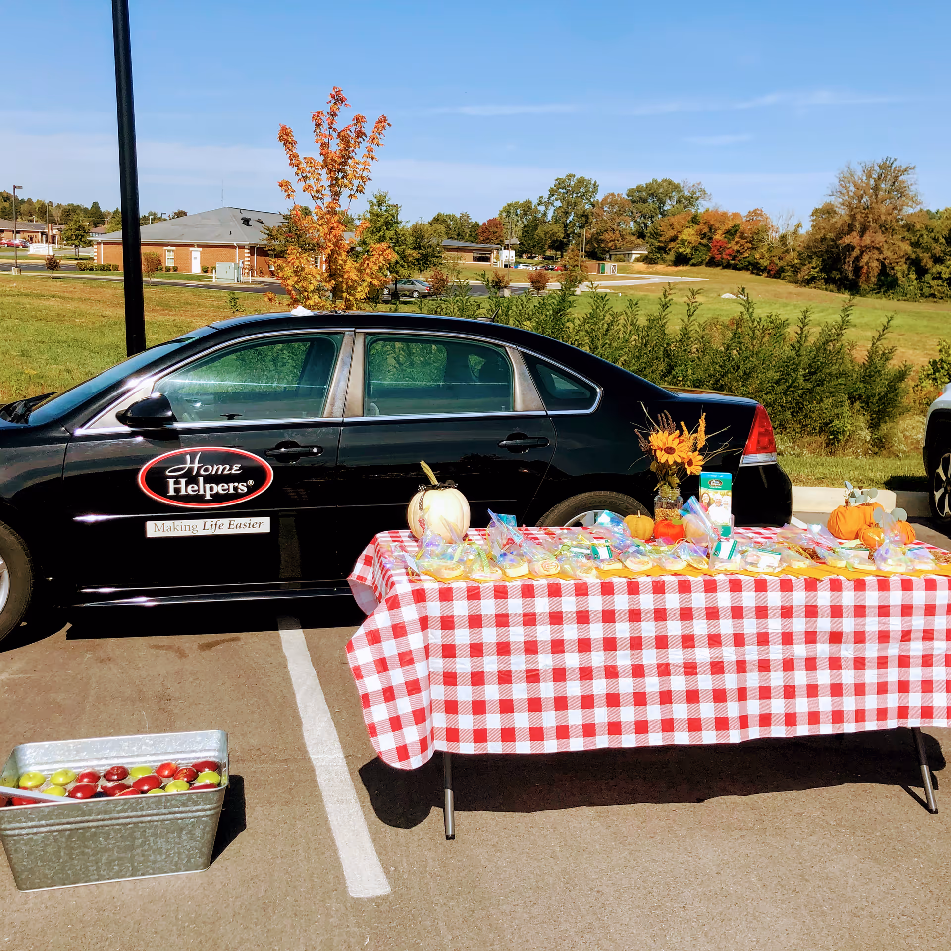 Table with red and white checkered cloth beside a Home Helpers car in a parking lot