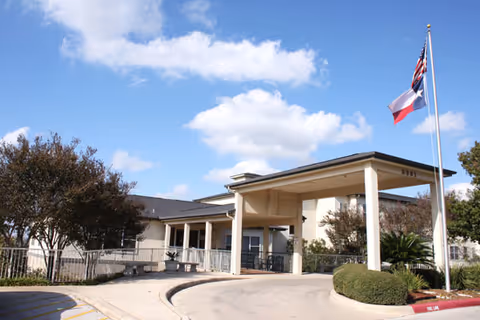 Entrance to a senior living facility with a covered driveway and flagpole.