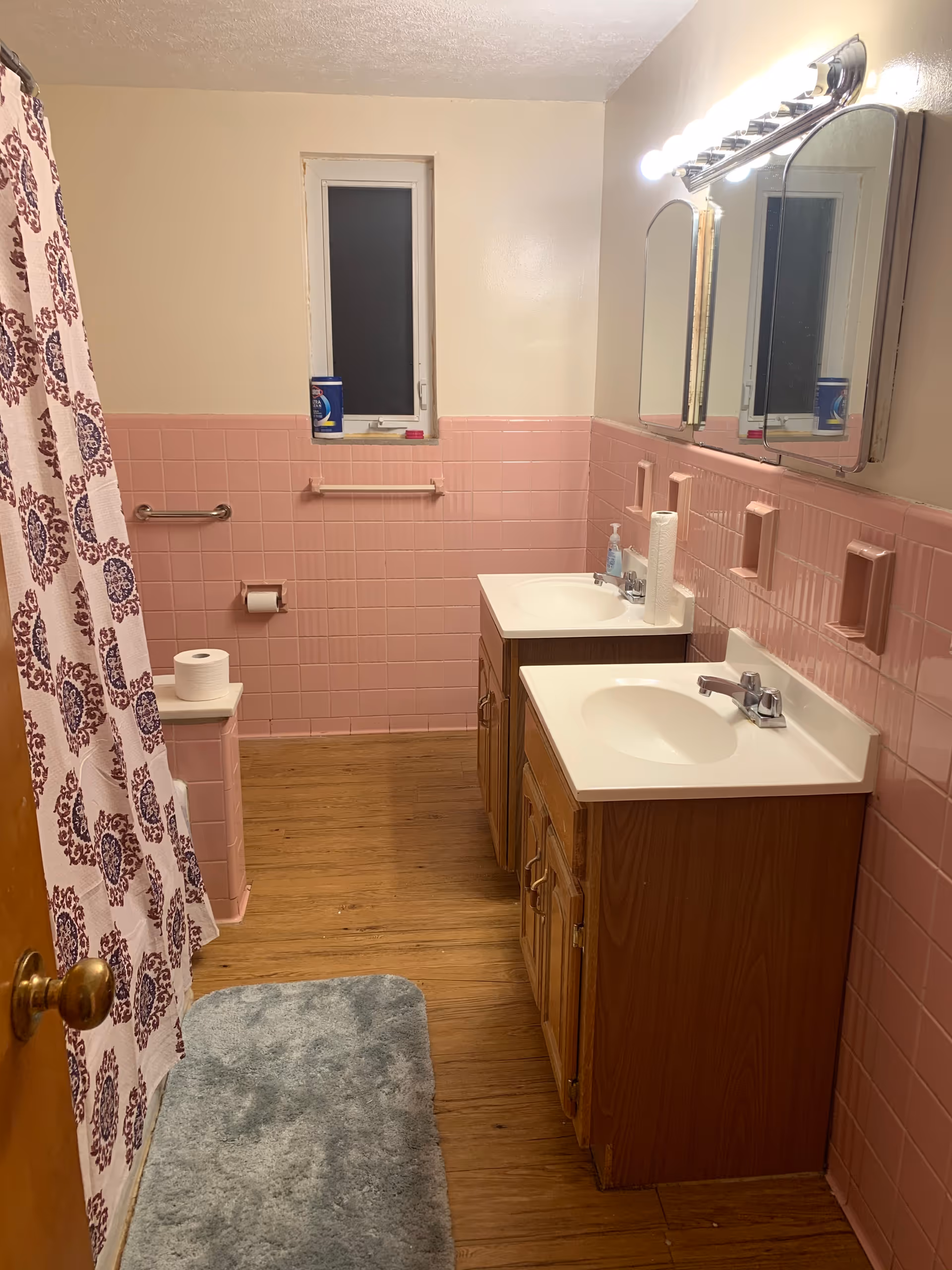 Pink-tiled bathroom with double sinks, mirrors, shower curtain, and wooden vanity.