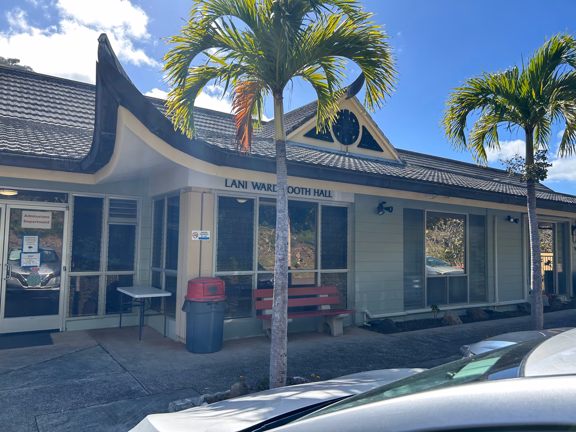 Exterior view of Palolo Chinese Home Lani Ward Booth Hall with palm trees and bench.