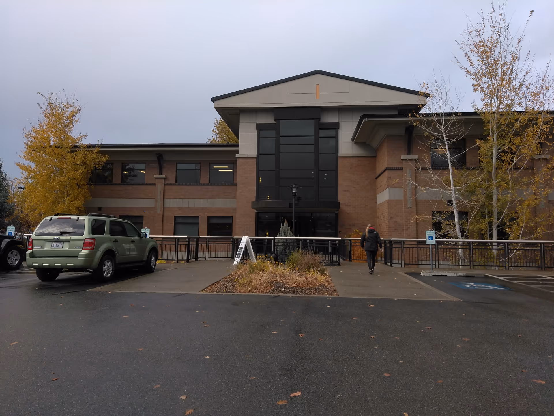 Front exterior of a brick senior facility with parking, ramps, and autumn trees.