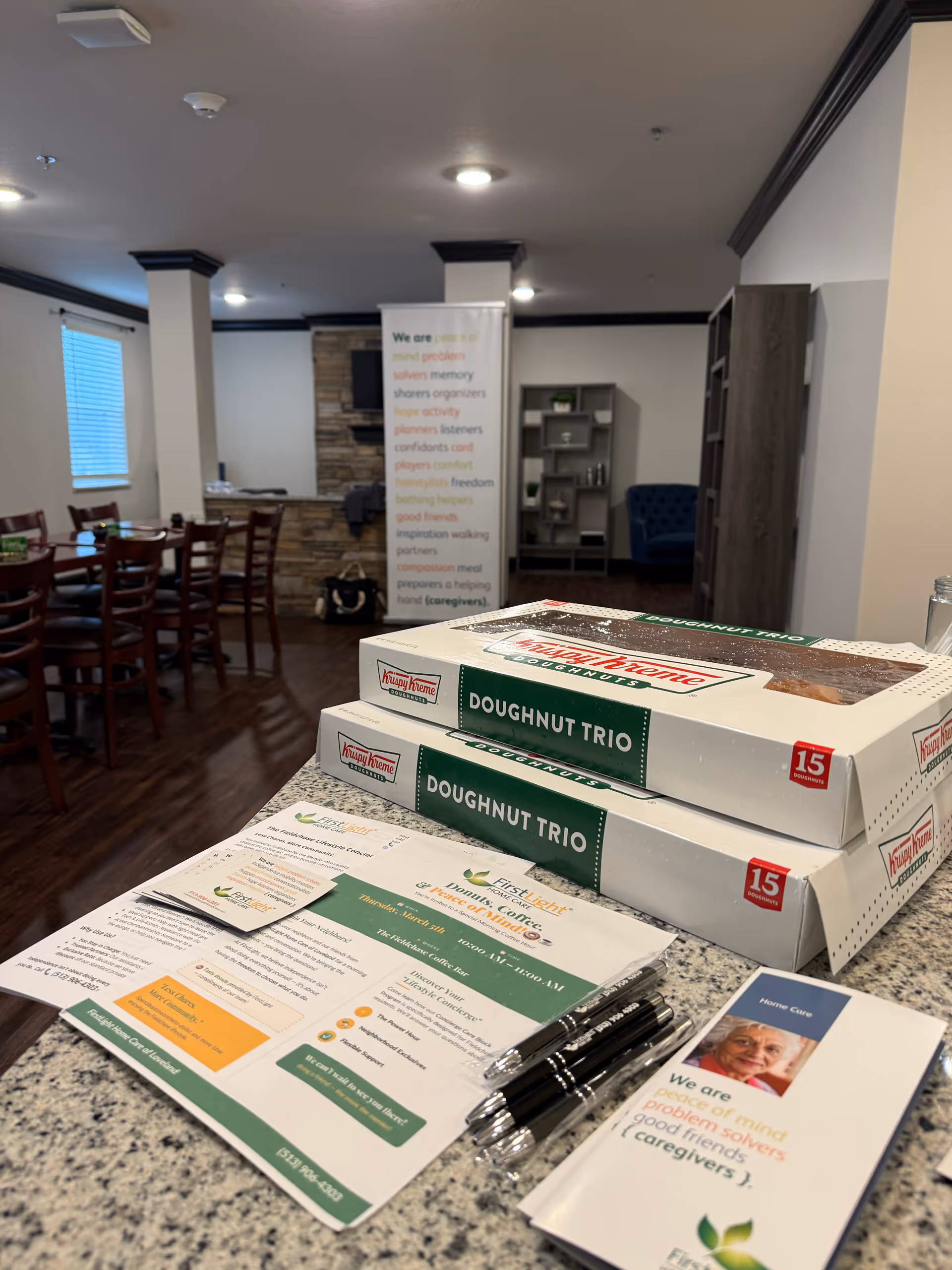 Indoor senior living lobby with doughnut boxes, brochures, and a dining area.