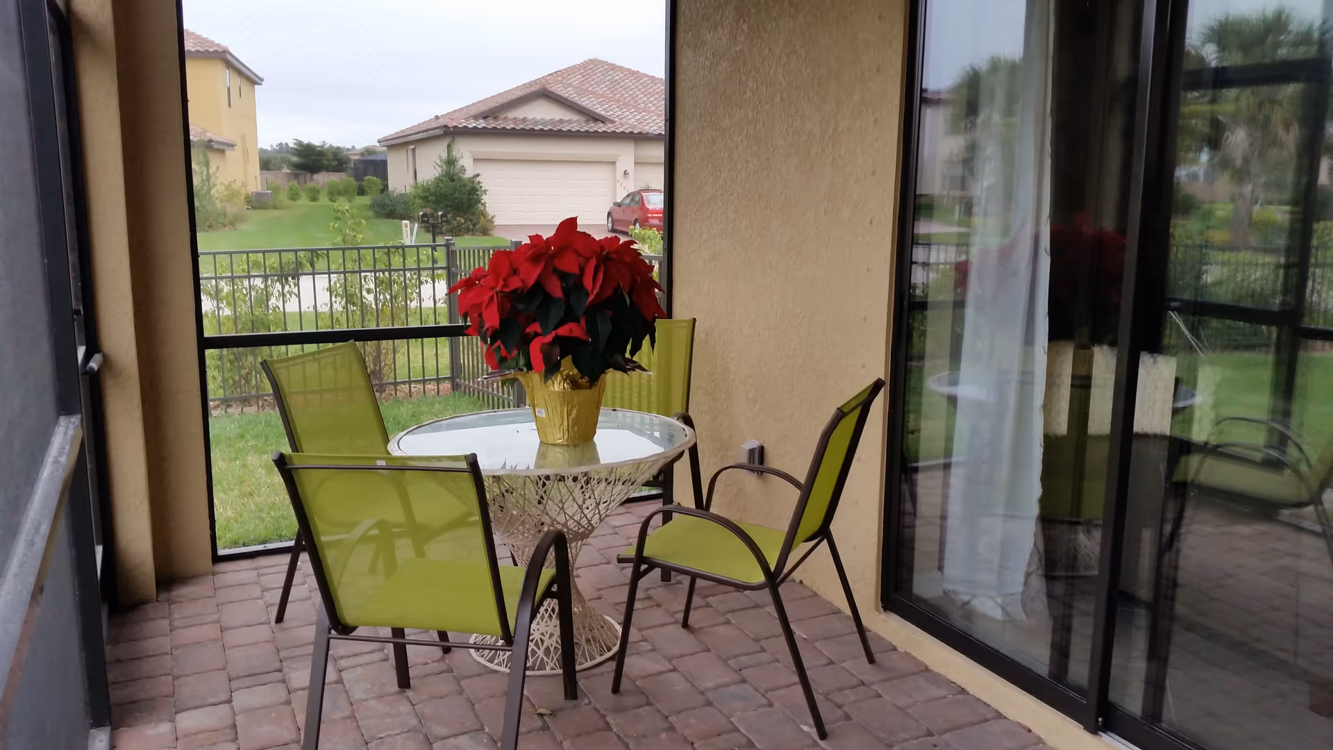 Screened patio with a round glass table, four green chairs and a red poinsettia, overlooking neighboring houses.