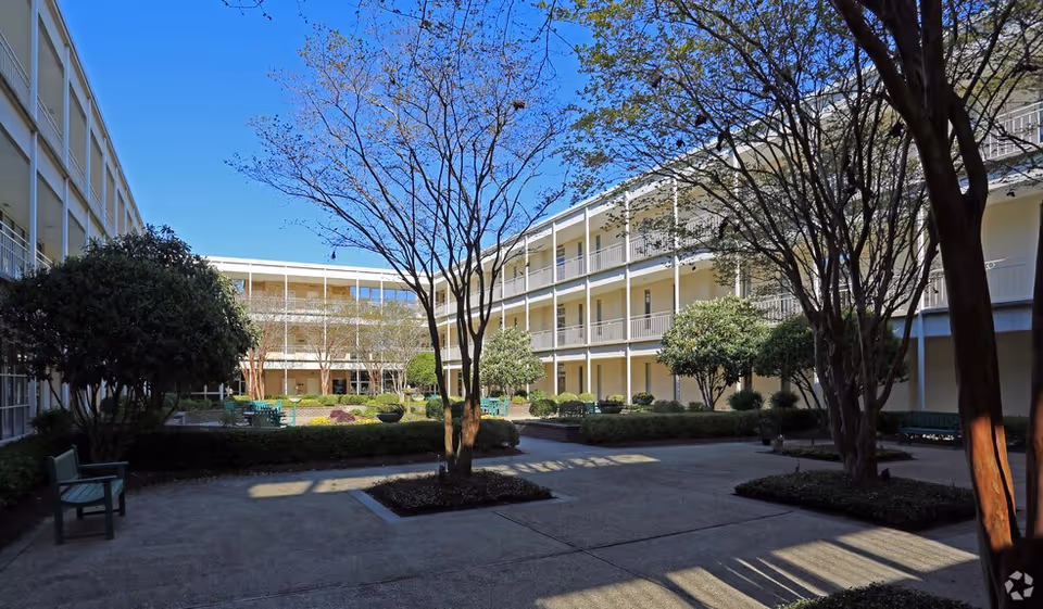 Sunny courtyard between two senior living wings with trees, hedges, and benches.