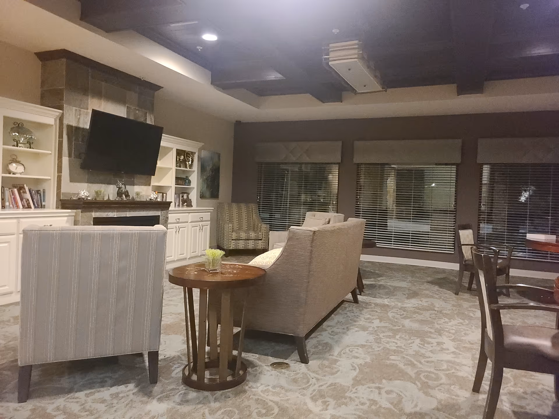 Cozy senior living lounge with sofas, a TV, fireplace, and large windows.