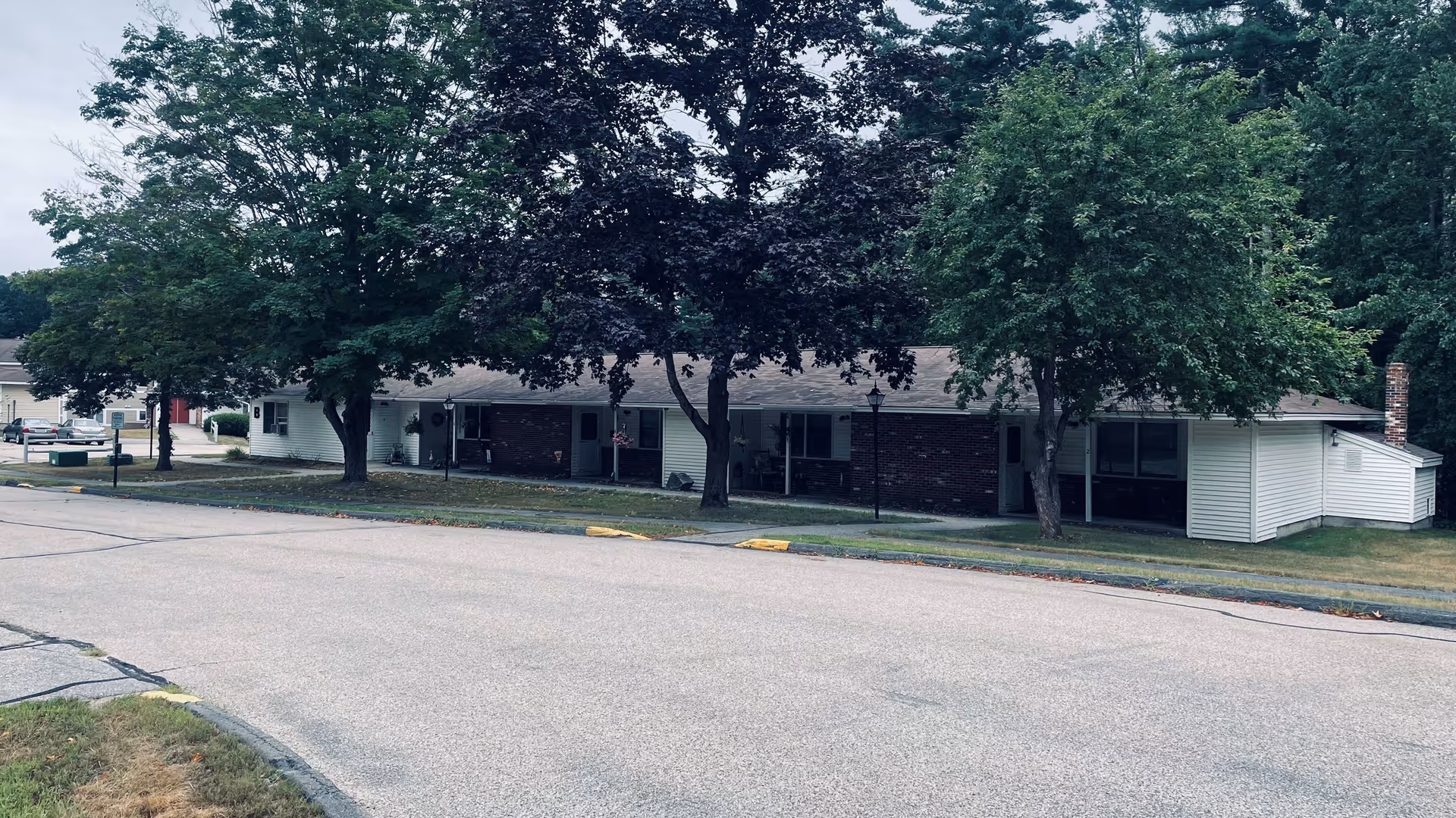 Pleasantwood Estates single-story building with brick, siding, front lawn, and large trees.