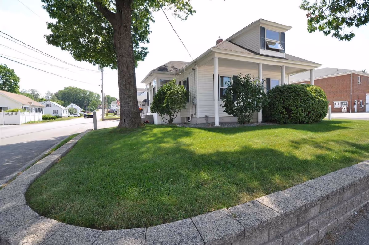 A small white house with a covered porch sits on a well-kept lawn.