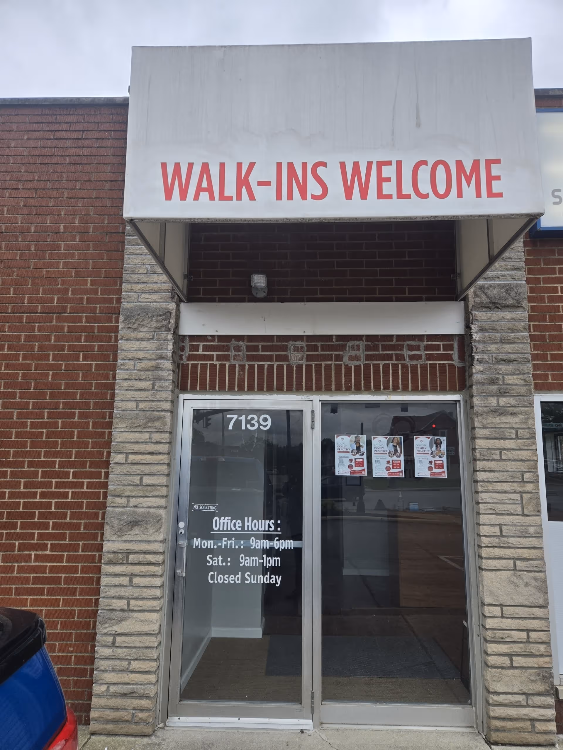 Front entrance of a brick building with a large WALK-INS WELCOME sign above glass doors.