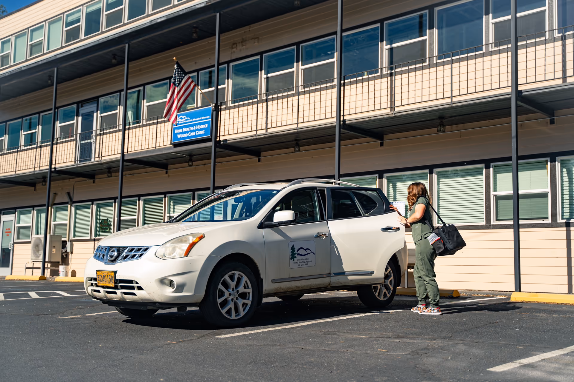 Exterior view of Blue Mountain Hospice building with a parked white SUV and a standing woman.