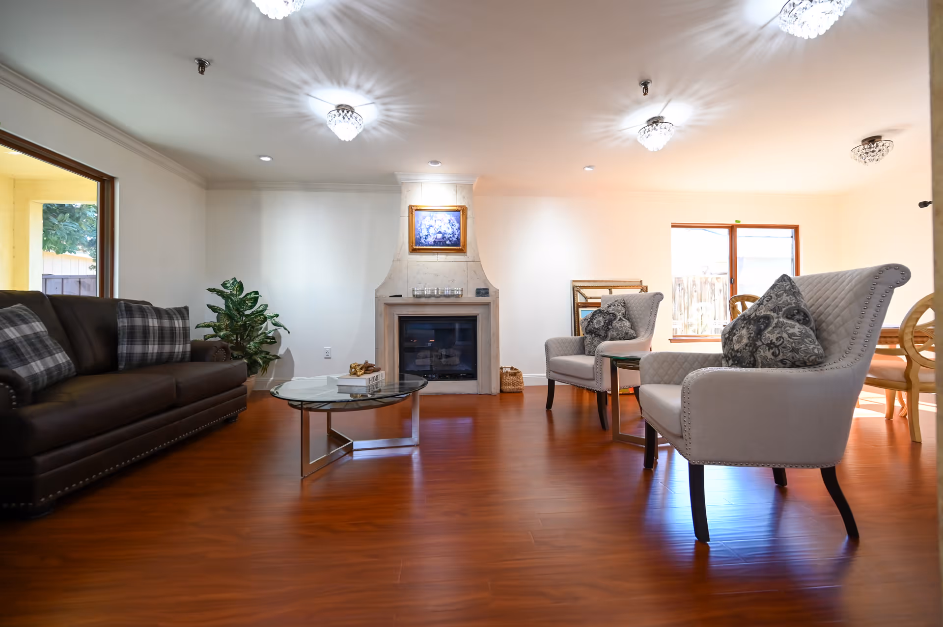 Bright living room with leather sofa, armchairs, fireplace, and glass coffee table.