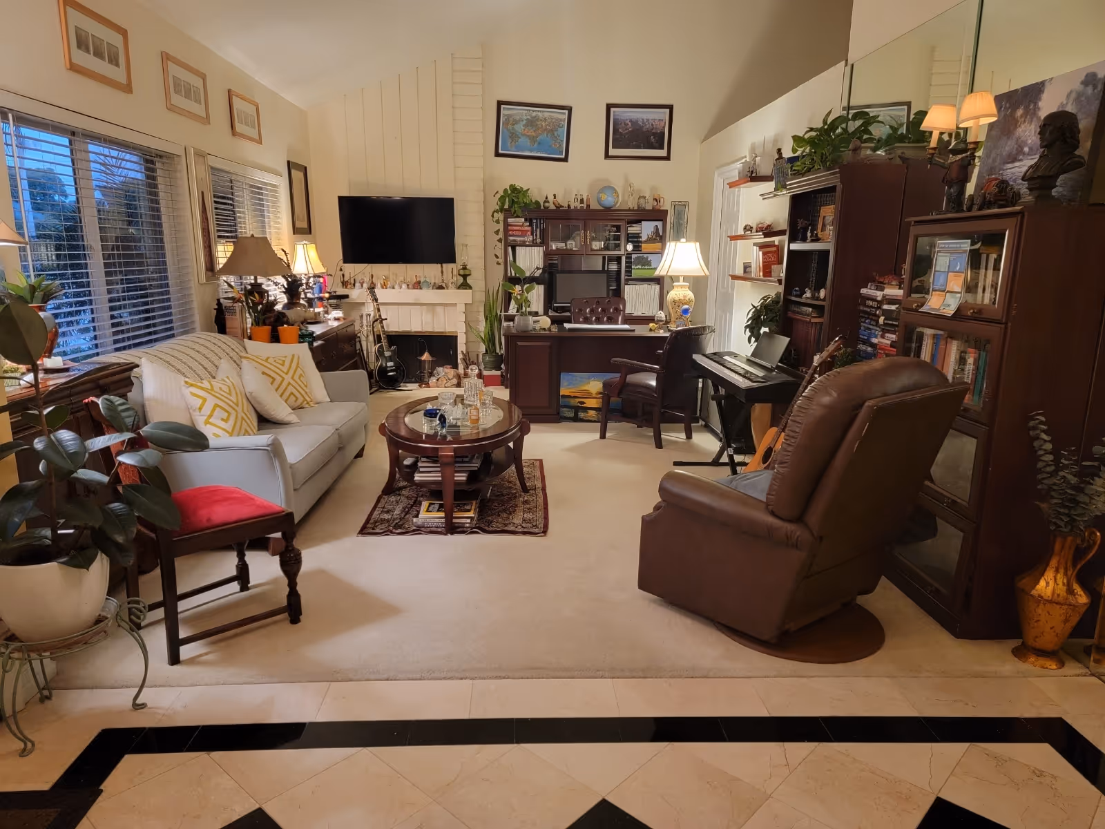 Cozy, well-decorated living room with a sofa, armchair, coffee table, TV above a fireplace, bookshelves and a desk.