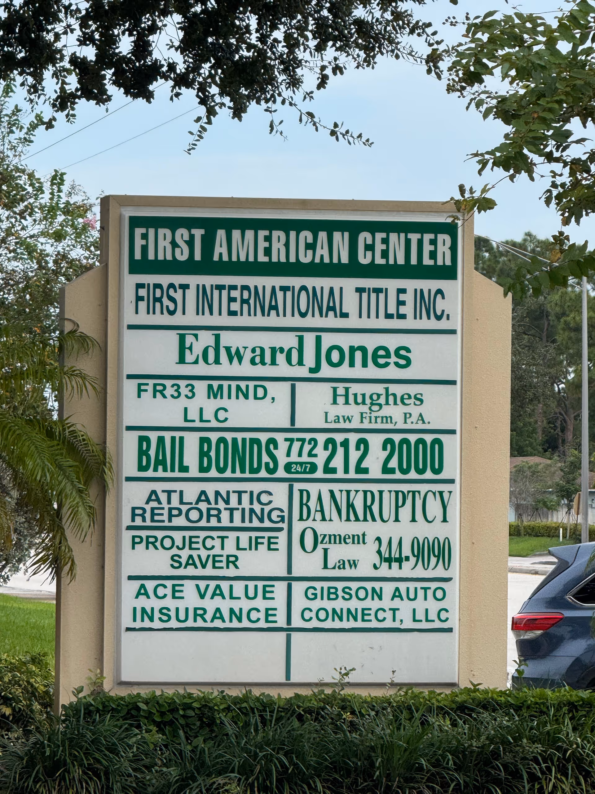 Outdoor signboard with multiple business names mounted on a landscaped building front.