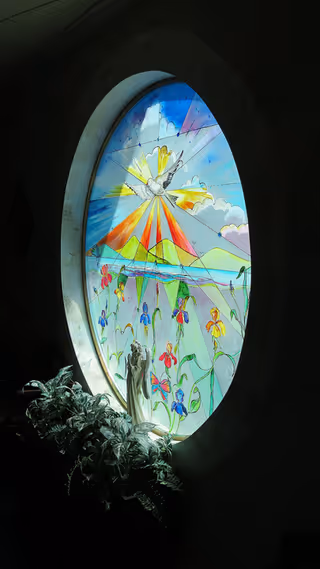 Circular stained-glass window with colorful floral scene in a dark interior.