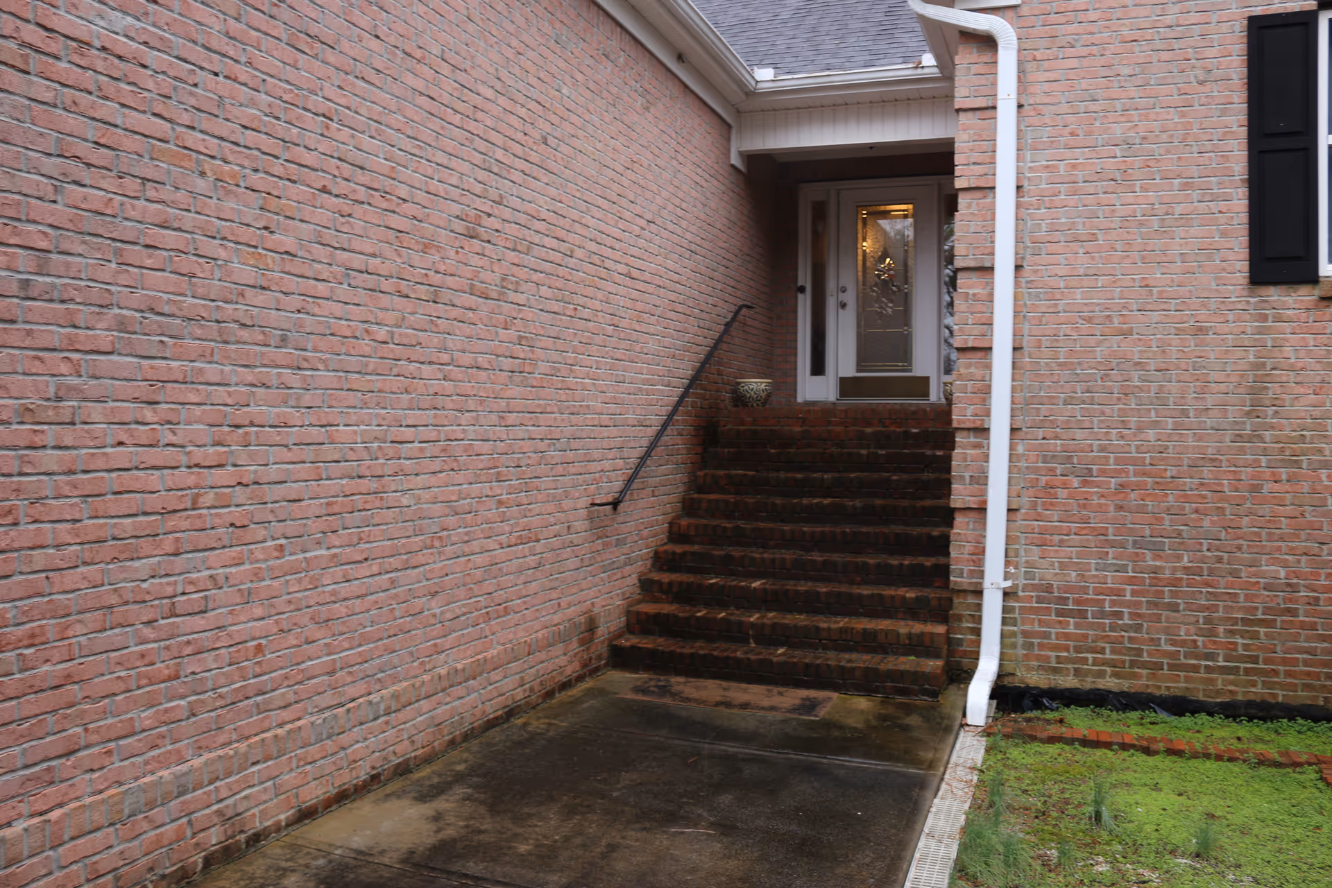 Brick exterior with stairway to glass door entrance, downspout, and a potted plant.