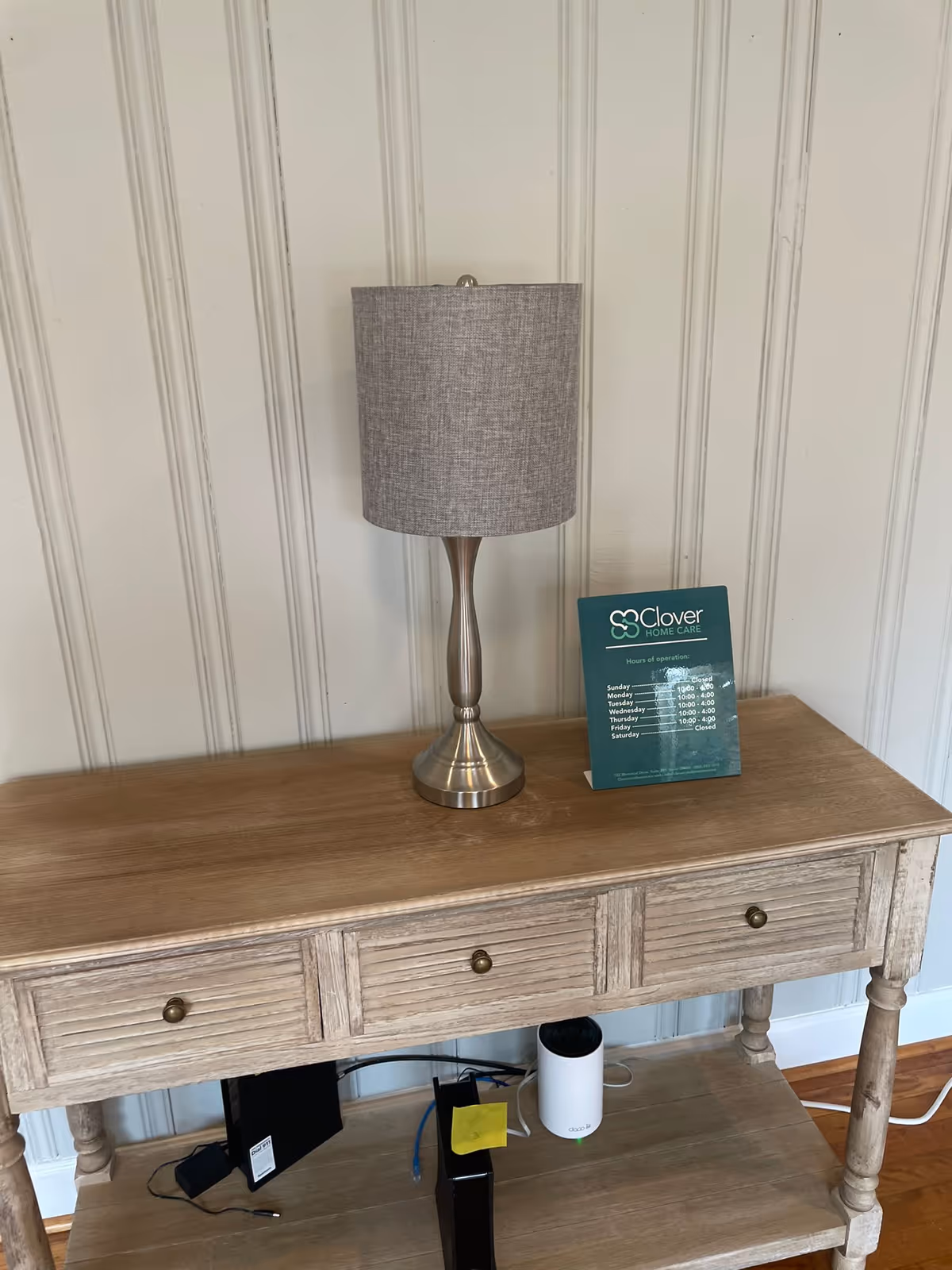 A wooden console table with a grey lamp on a paneled interior wall.