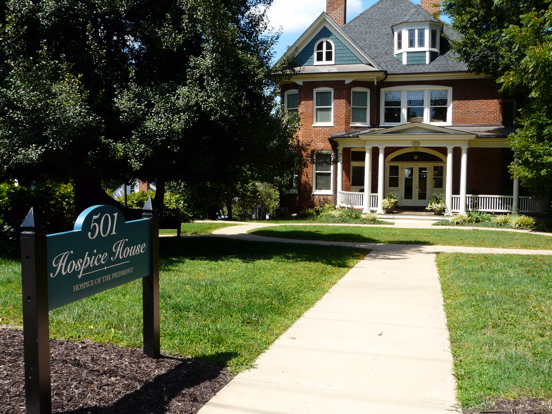 Brick Hospice House front with porch, sign, and a central walkway.