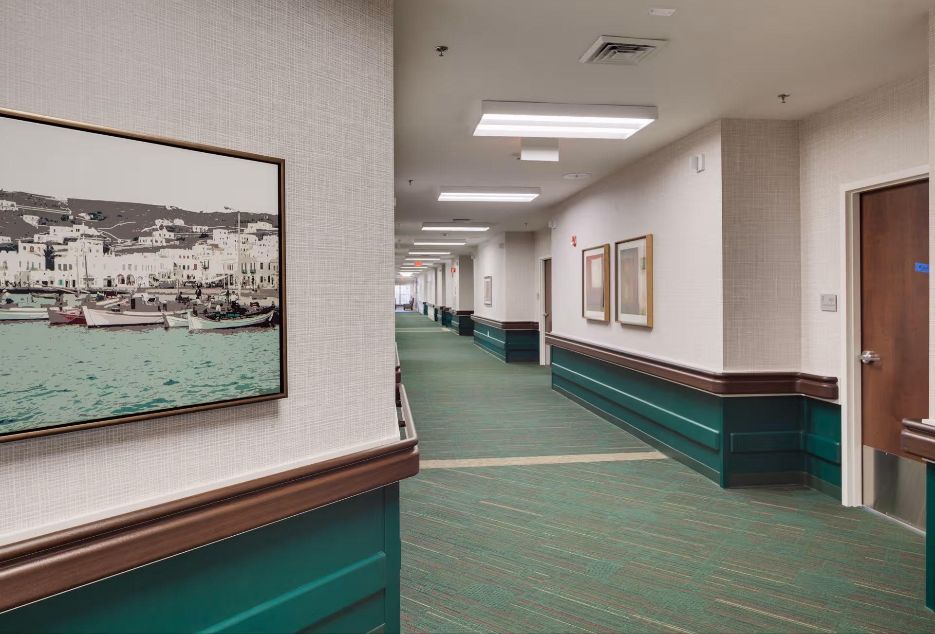 Bright interior hallway of a senior living facility with framed artwork and green wainscoting.