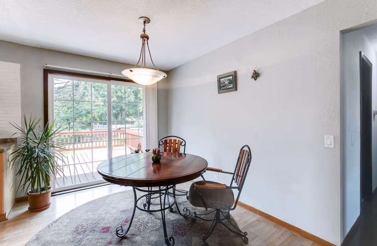 Round wooden dining table with chairs in a bright interior dining area by a sliding door.