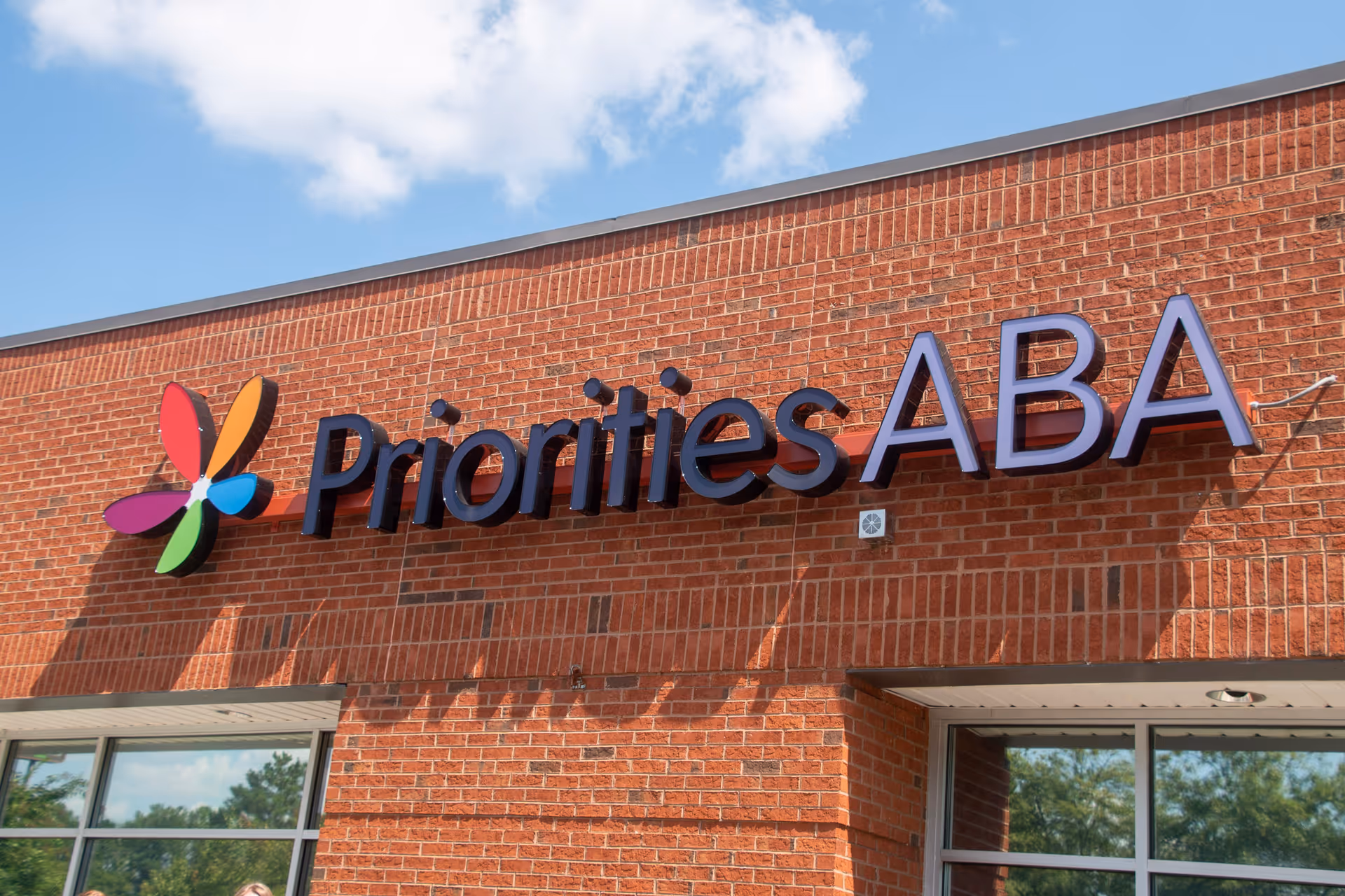 Red brick building exterior featuring a large Priorities ABA sign and colorful logo.