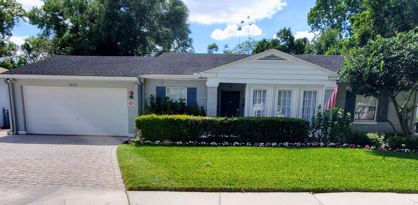 Single-story facility exterior with a two-car garage, manicured lawn, and flowering shrubs.