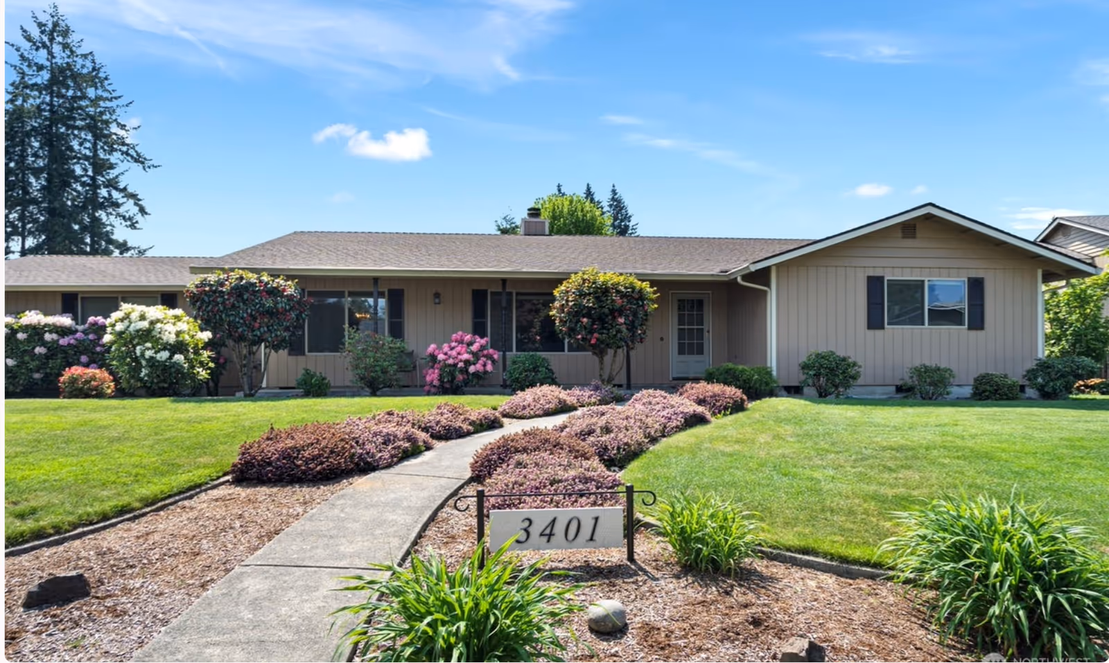 A single-story beige building with a manicured front yard, walkway, and landscaped shrubs.