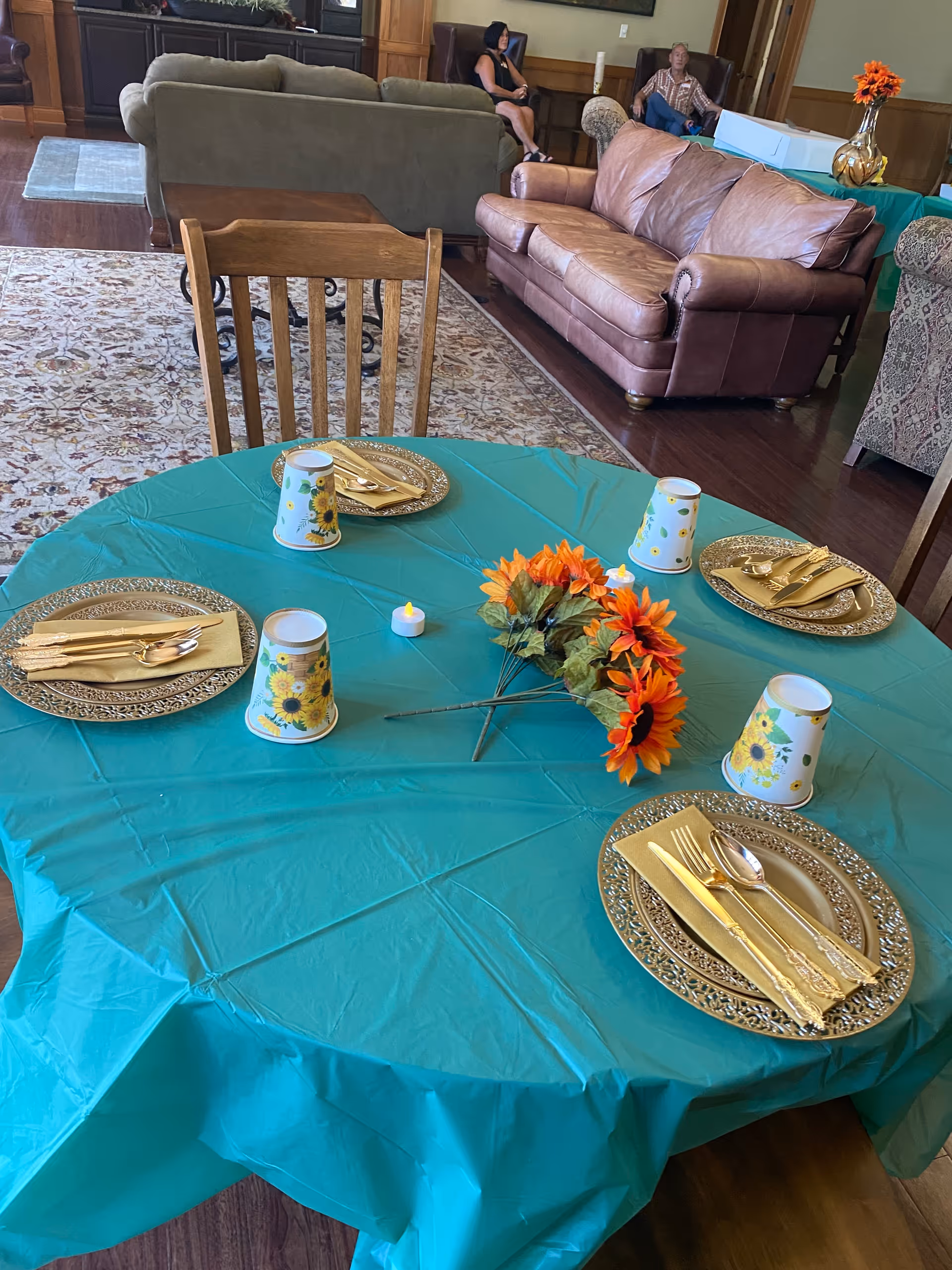 Round teal table set for a meal with sunflowers in a senior living lounge.