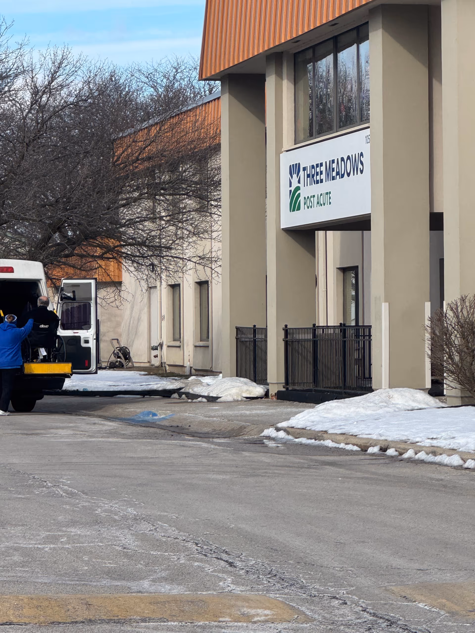 Exterior view of a facility entrance with a Three Meadows Post Acute sign and a van.