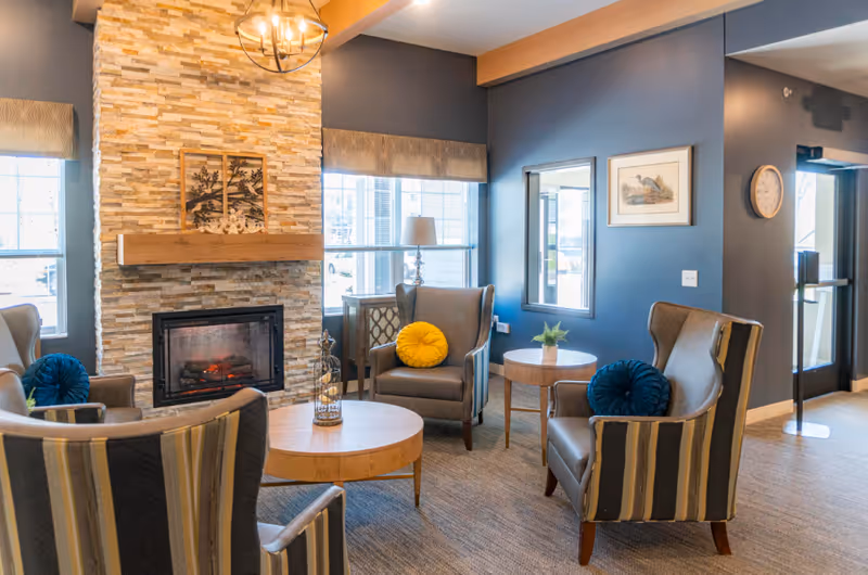 Cozy lounge with a stone fireplace, blue walls, and striped armchairs.