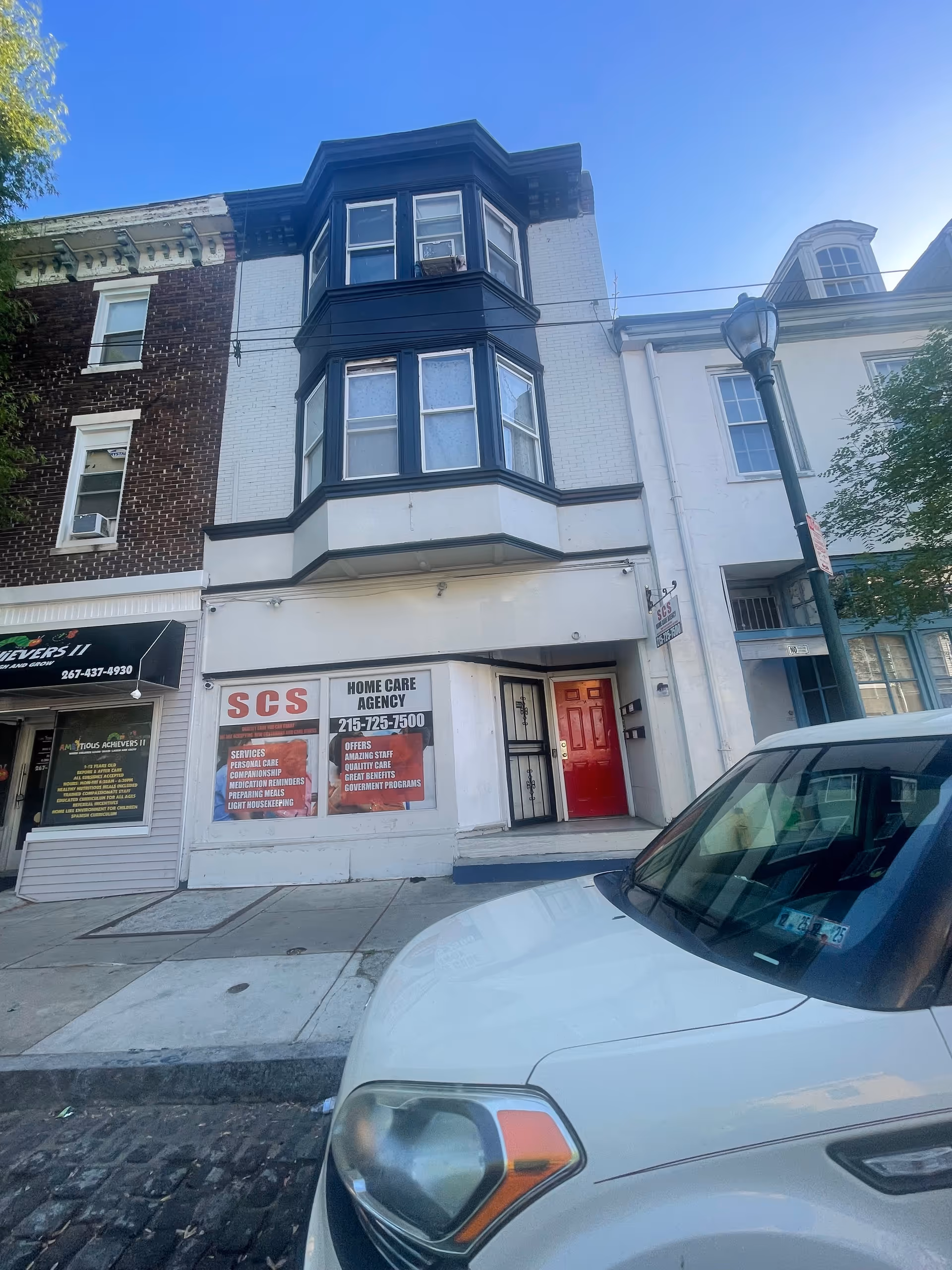 Three-story building with a red door and SCS Home Care Agency sign on storefront.
