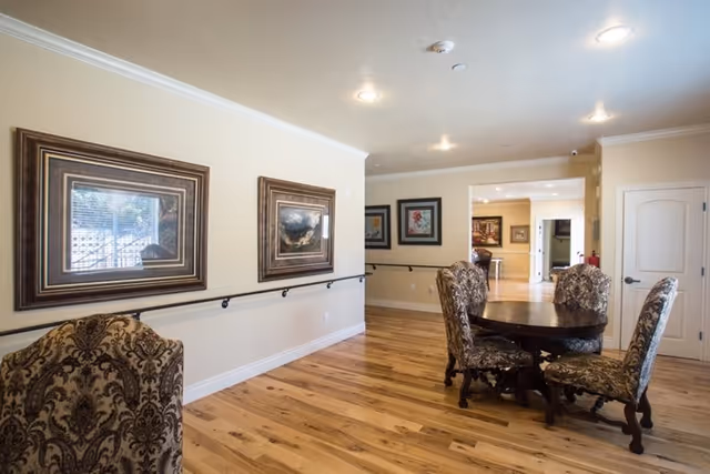 Wide hallway with framed art on cream walls and a round dining table with upholstered chairs.