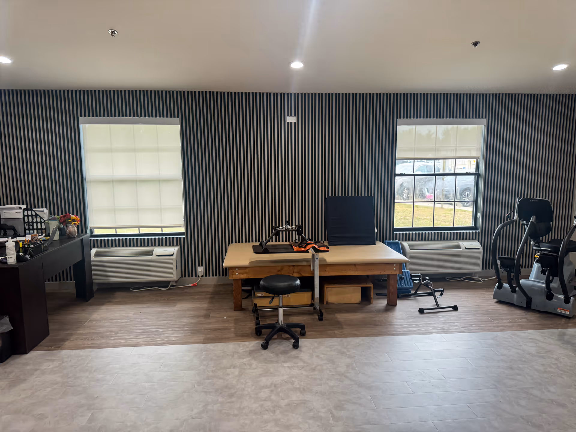 Interior rehab/therapy room with striped walls, exercise equipment, a table, and chairs.