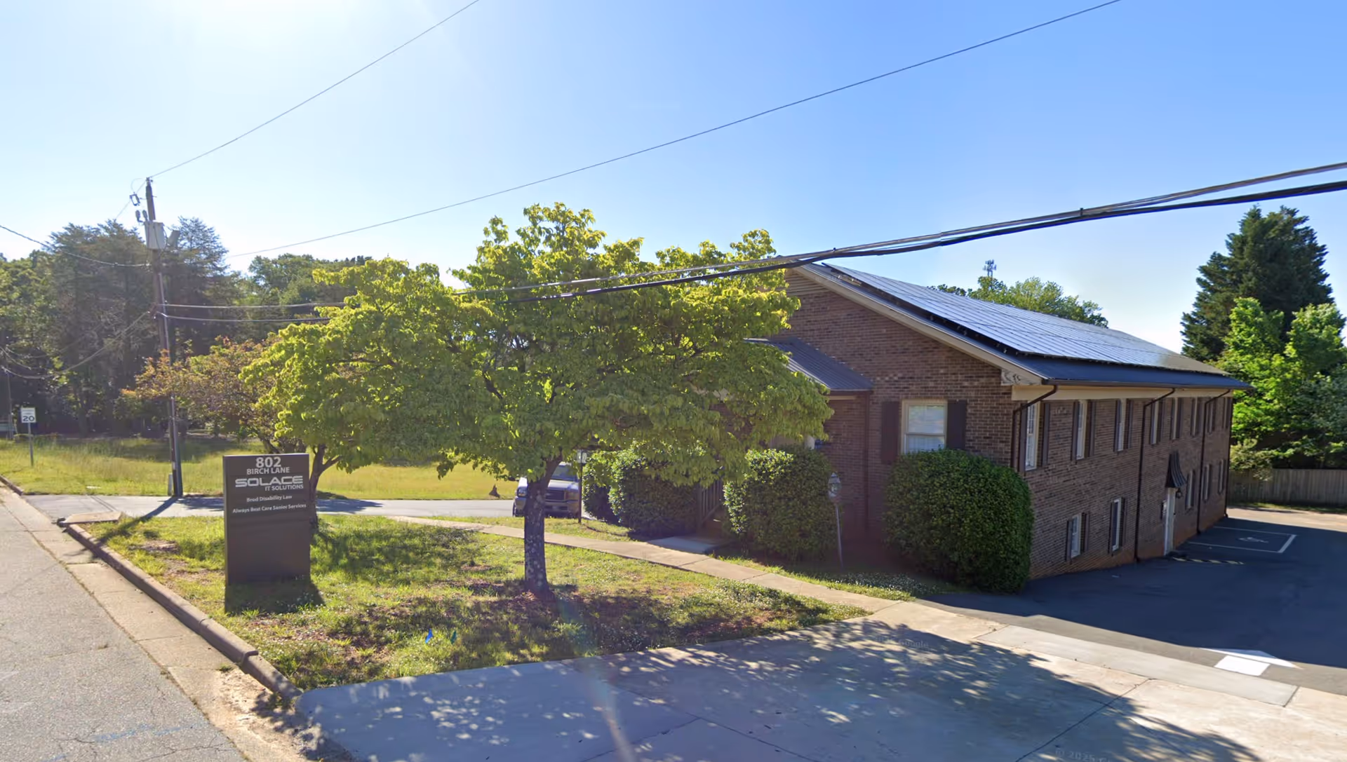 A brick senior care building with a tree, sign, and parking along a quiet street.