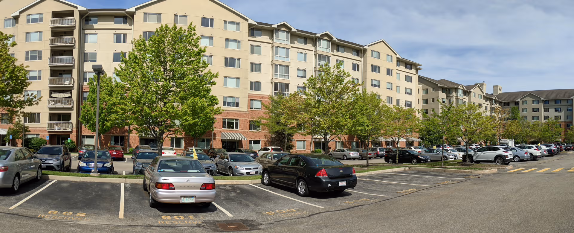 Exterior view of a multi-story senior living building with a tree-lined parking lot.