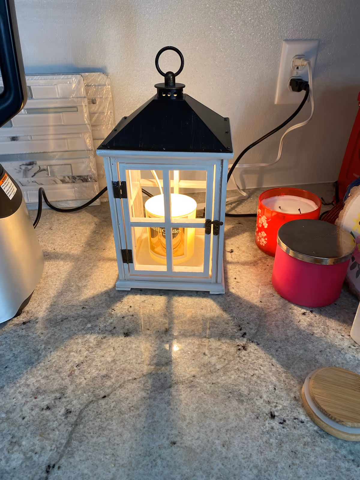 A white lantern with a glowing candle sits on a granite kitchen counter.