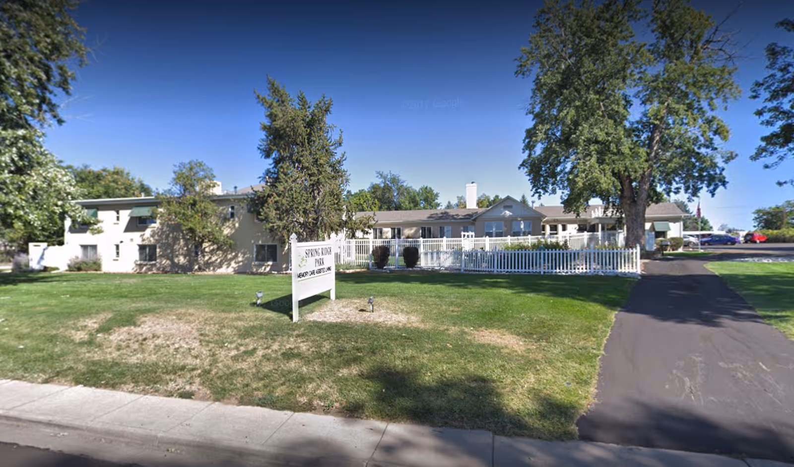 Front view of Spring Ridge Park Assisted Living with a white fence and green lawn.