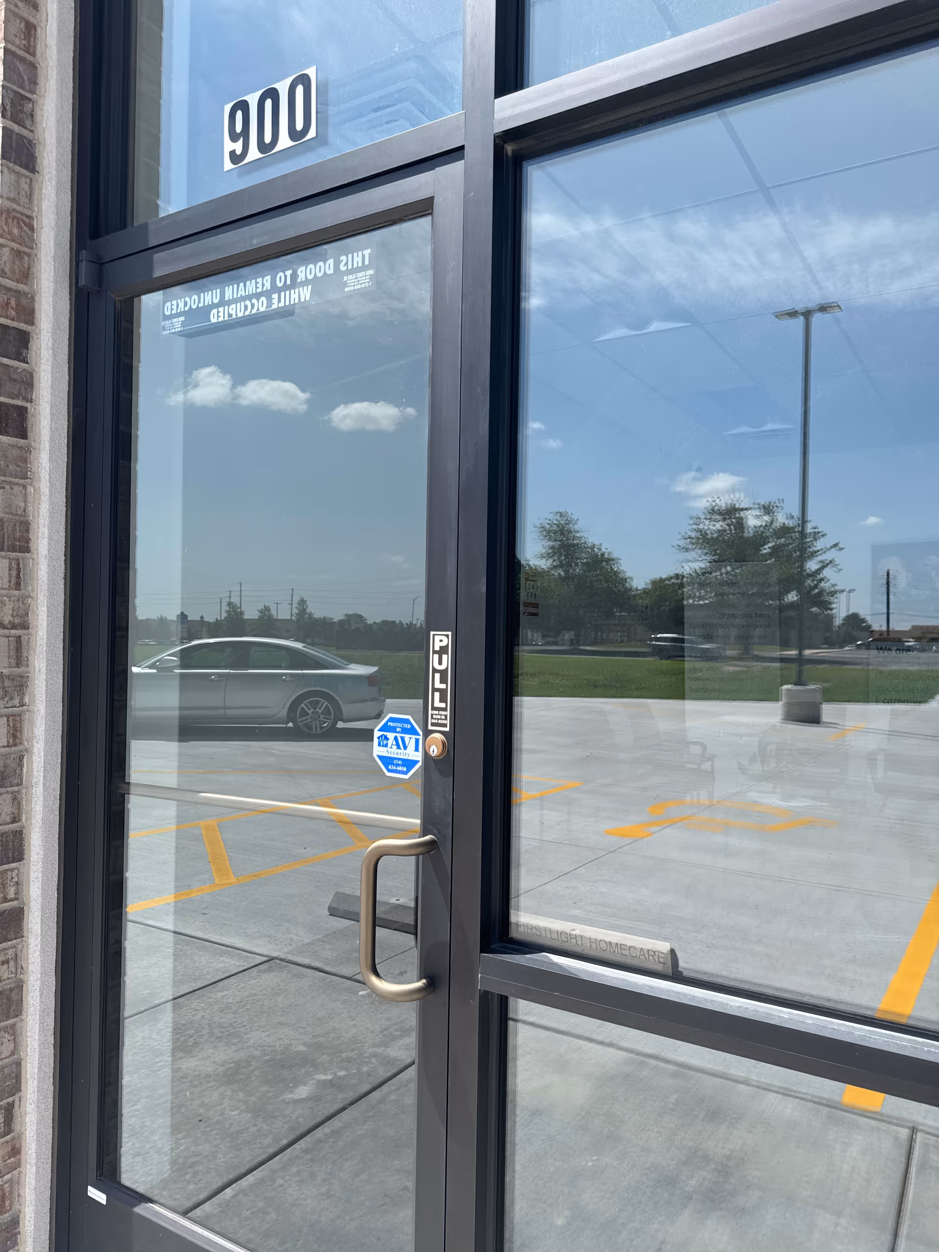 Glass entrance door labeled 900 with a pull handle, reflecting parking lot and sky.